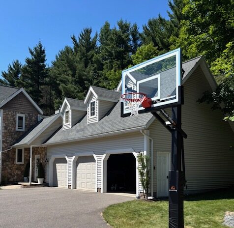 An in-ground 60-inch adjustable basketball hoop installed on a residential driveway next to a garage